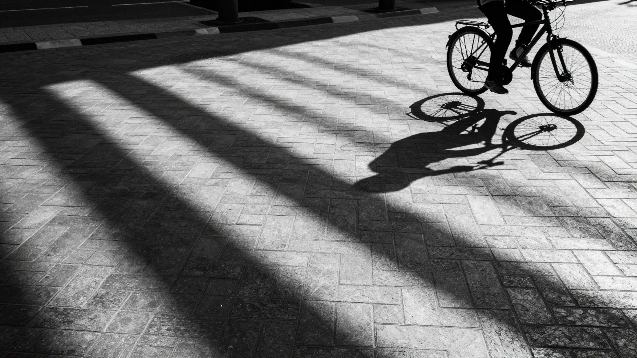 Diagonal shadows stripe across patterned pavement as a cyclist passes
