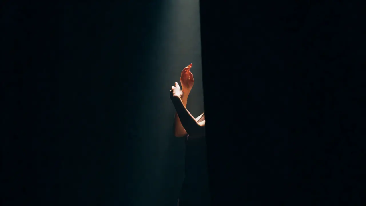 Dancer partially lit in spotlight surrounded by deep shadows